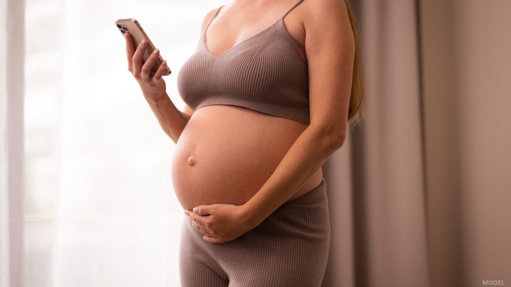 Pregnant woman researching on mobile phone (model)